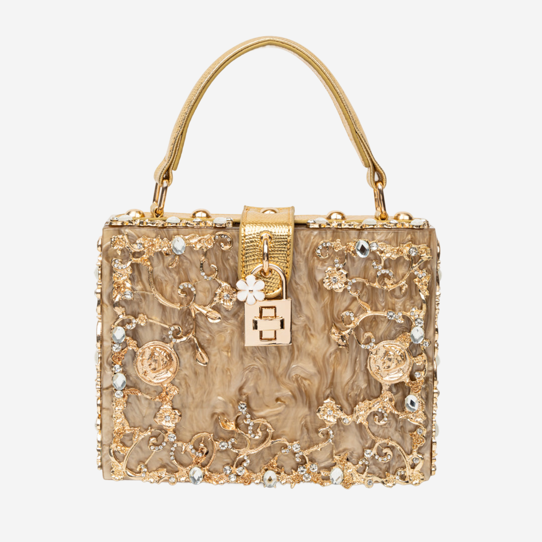 A gold-colored handbag with intricate floral and leaf designs, adorned with rhinestones and a lock-like clasp.