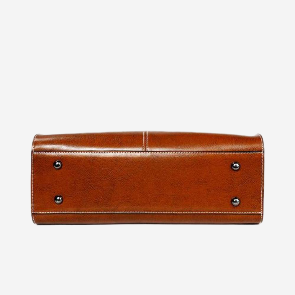 A brown leather handbag with a curved top and two metal studs on the bottom.