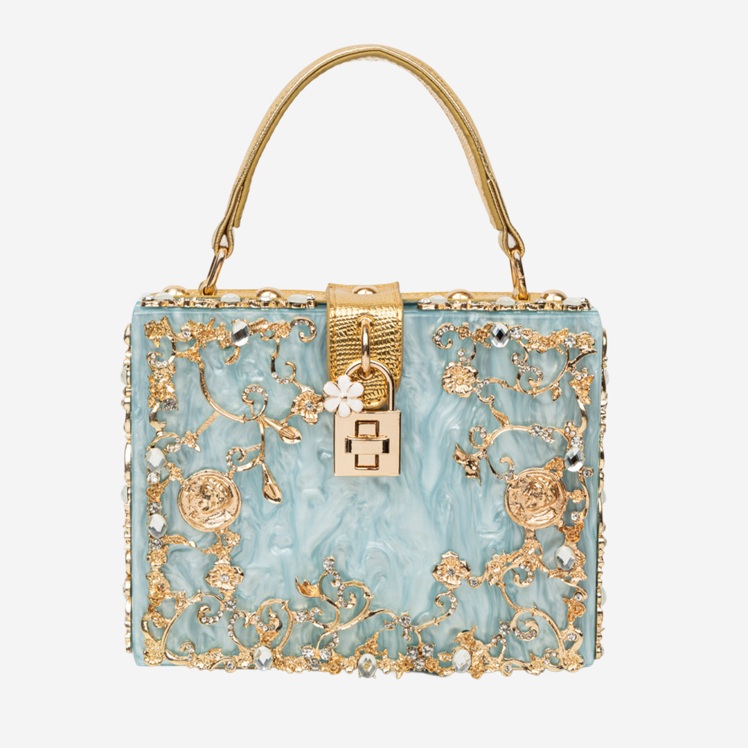 A handbag with a blue and gold color scheme, adorned with intricate floral and leaf designs, and embellished with rhinestones and a lock-like clasp.