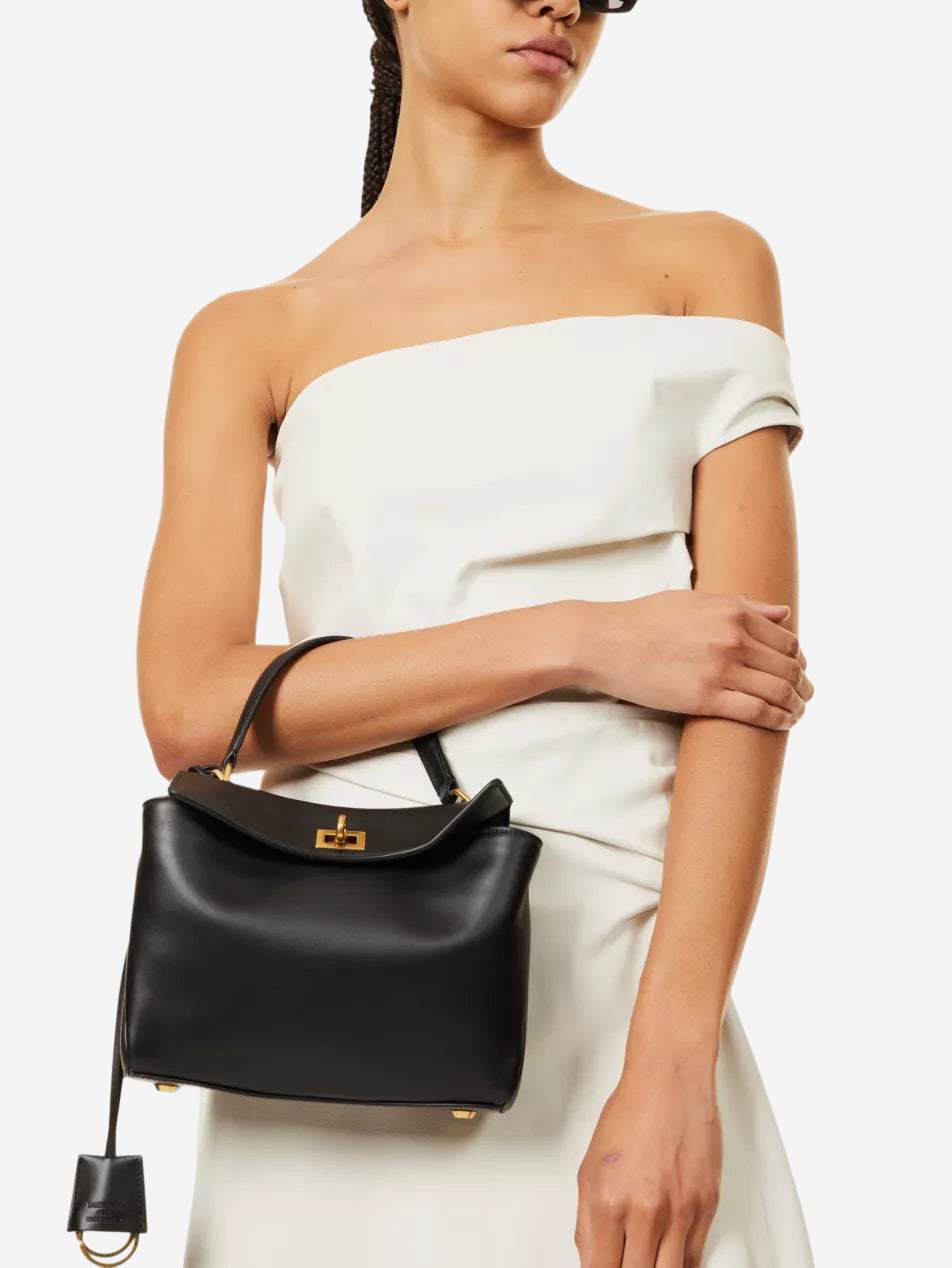 A woman wearing a white off-the-shoulder dress and holding a black leather handbag.