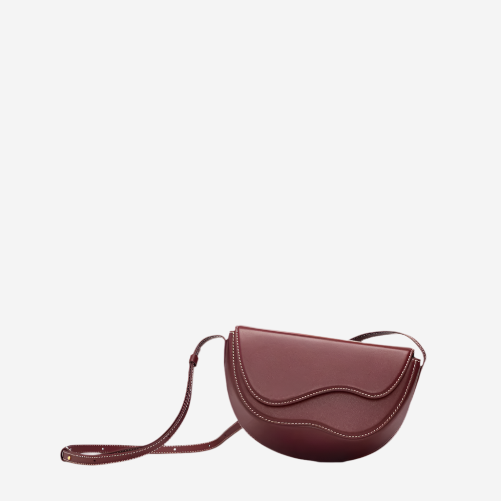 A burgundy-colored handbag with a curved shape and a strap, sitting on a white background.