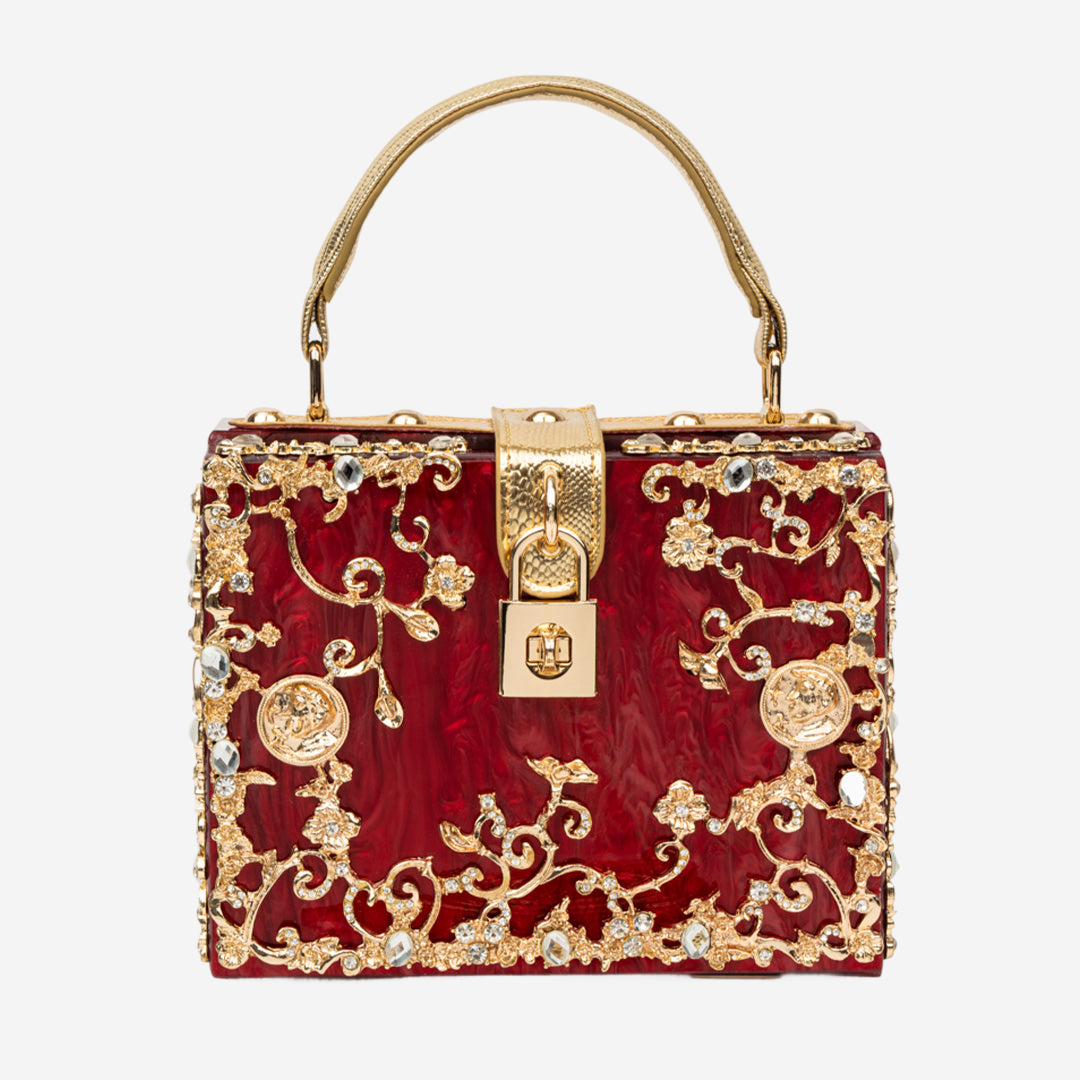 A red handbag with gold floral and crystal embellishments, including a lock-shaped clasp and a gold handle.