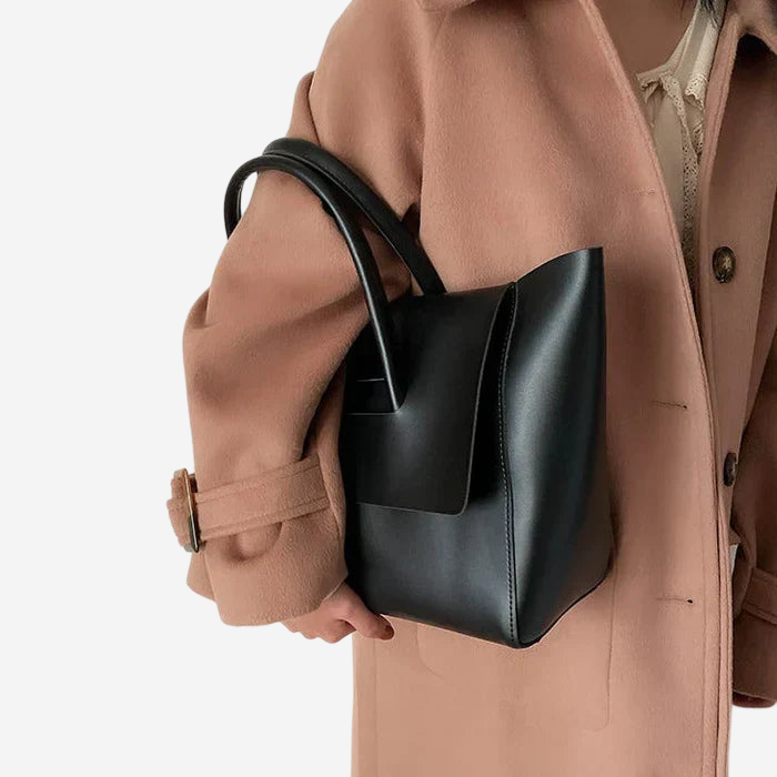 A person wearing a tan coat and carrying a black leather handbag.