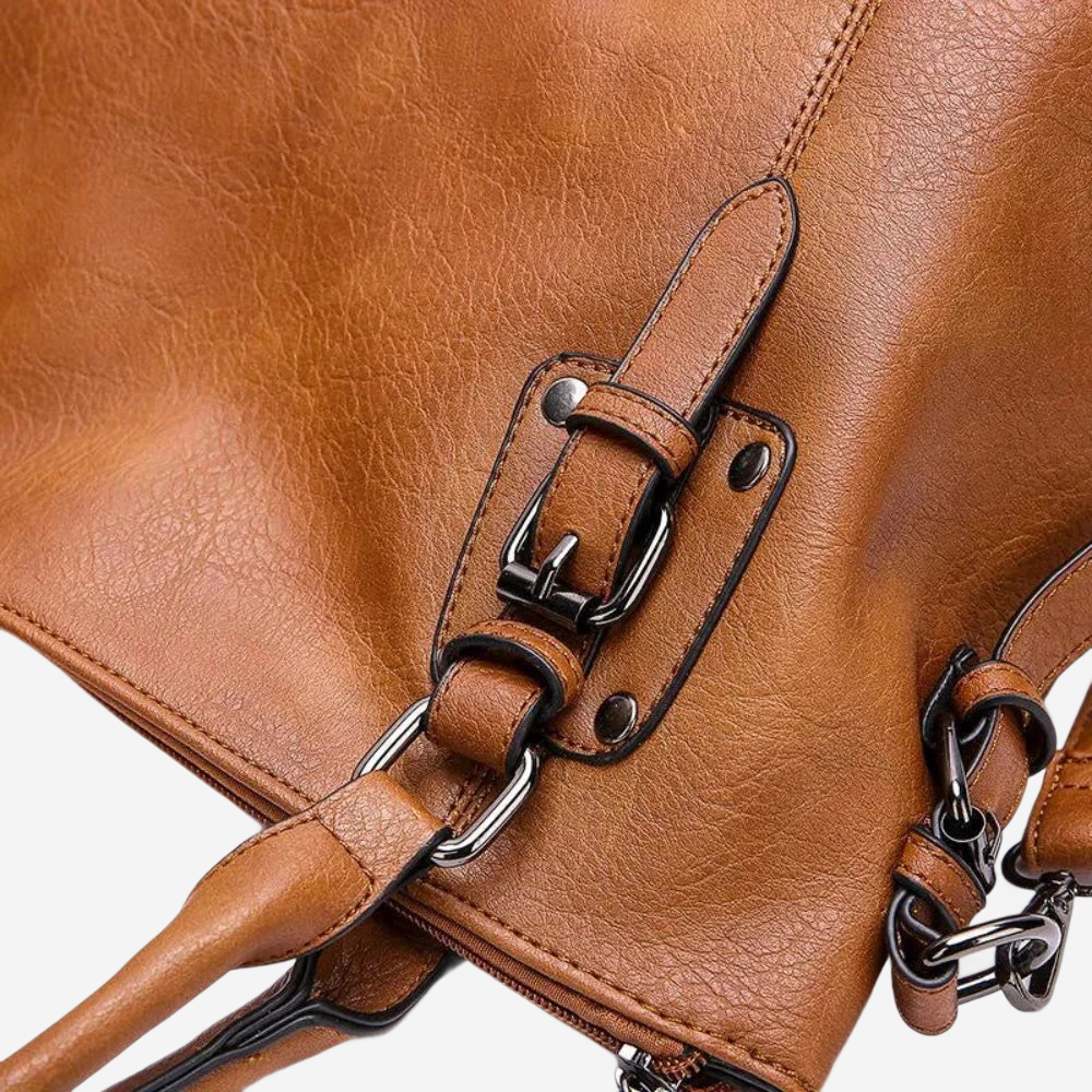 A close-up view of a brown leather handbag with metal hardware, including a buckle and zipper.