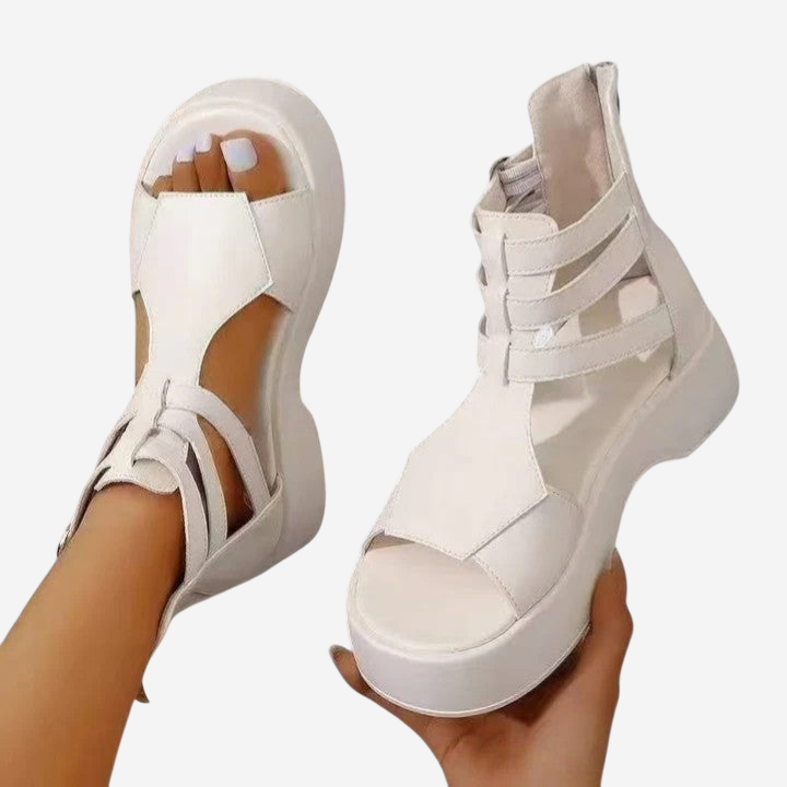 A pair of white platform sandals being held in a hand.