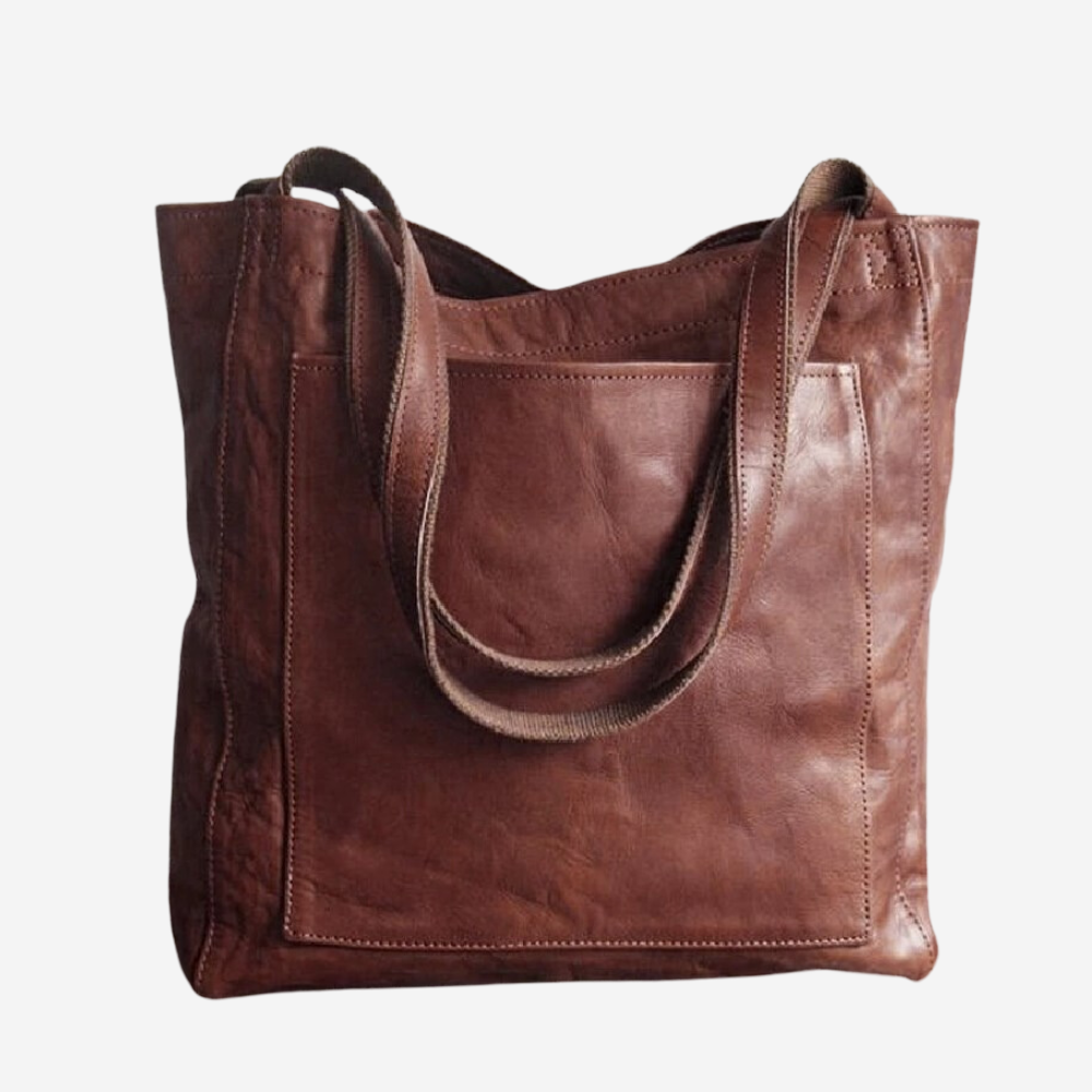 A brown leather tote bag with a strap and a pocket on the front.