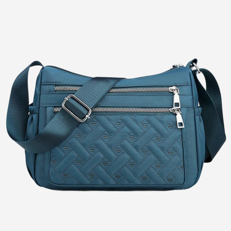 A blue crossbody bag with a quilted pattern and multiple zippers.