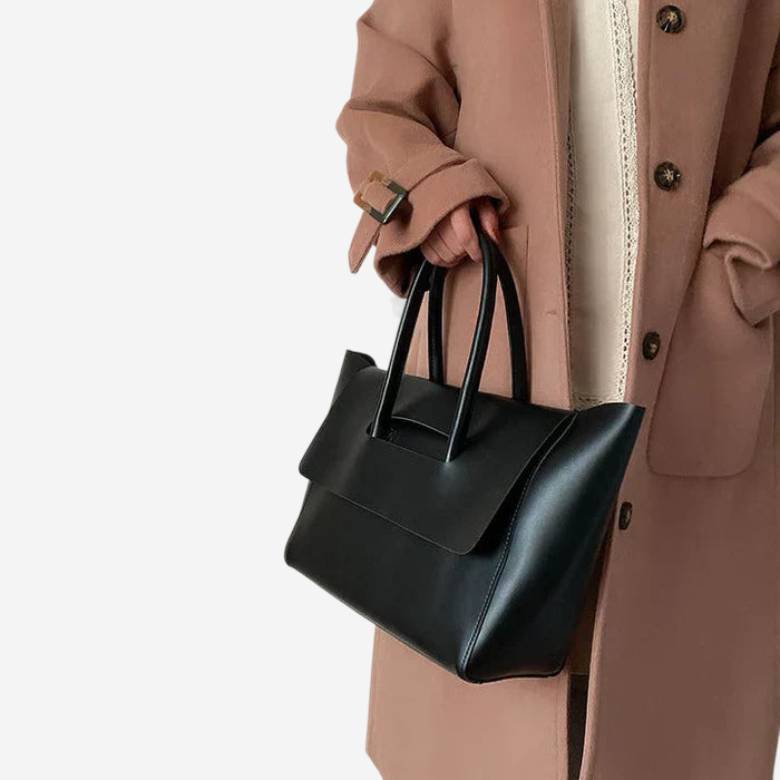 A person wearing a brown coat is holding a black handbag.