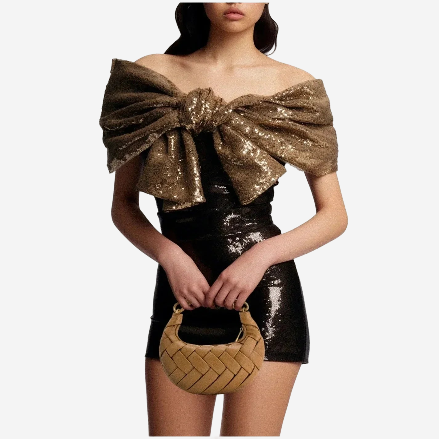 A woman wearing a black sequined dress with a large bow on the shoulder, holding a small woven purse.