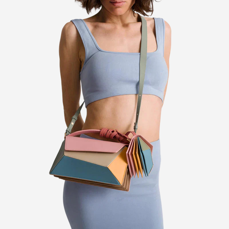 A woman wearing a blue crop top and holding a colorful geometric handbag.
