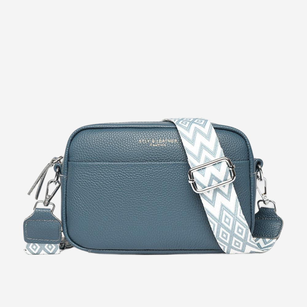 A blue leather crossbody bag with a geometric patterned strap.
