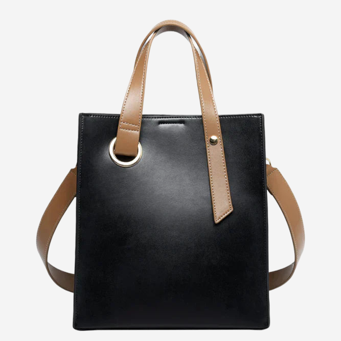 A black leather tote bag with a brown leather strap and a gold-tone metal ring on the front.