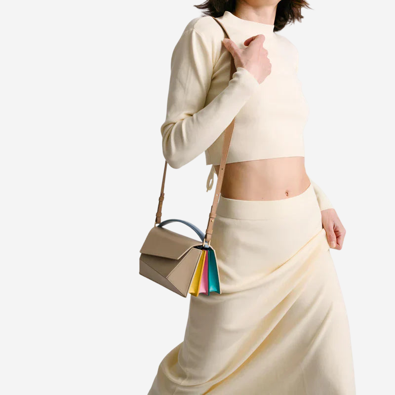 A woman wearing a white top and skirt is holding a small, beige handbag with a colorful strap.