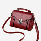A red leather handbag with a metal clasp and handle, featuring a curved front and two side pockets.