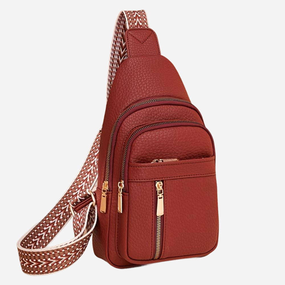 A red leather crossbody bag with multiple zippers and a patterned strap.