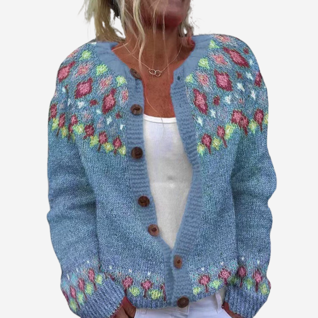 A woman wearing a blue knitted cardigan with colorful floral patterns.