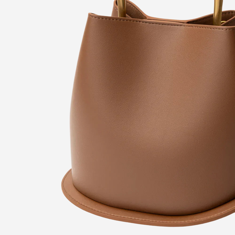 A close-up view of a brown leather handbag with a curved shape and a small handle.