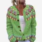 A woman wearing a green knitted cardigan with colorful floral patterns on the front.